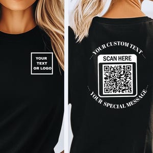 May include: Black t-shirt with white text and a QR code design. The front of the shirt has a white box with the words "YOUR TEXT OR LOGO". The back of the shirt has a QR code with the words "YOUR CUSTOM TEXT", "SCAN HERE", and "YOUR SPECIAL MESSAGE".