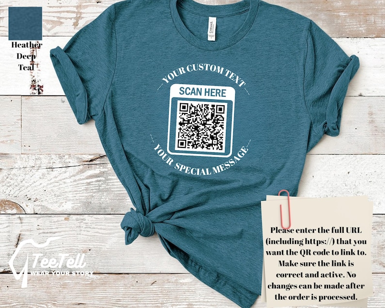 May include: Teal t-shirt with a QR code graphic. The shirt has the text "YOUR CUSTOM TEXT" above the QR code and "YOUR SPECIAL MESSAGE" below it. The text "SCAN HERE" is above the QR code. A note attached to the shirt says to enter the full URL for the QR code.
