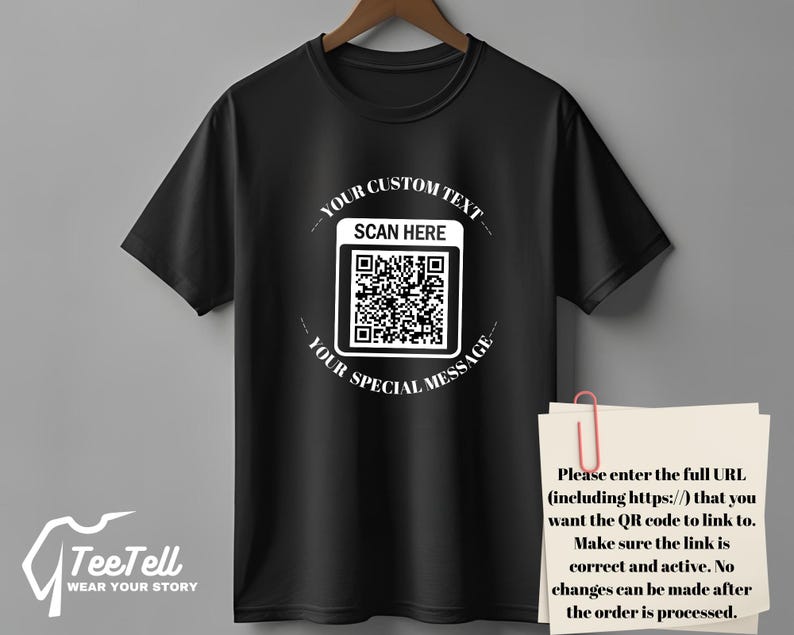 May include: Black t-shirt with a QR code design. The shirt has the text "YOUR CUSTOM TEXT" and "YOUR SPECIAL MESSAGE" around the QR code. The text "SCAN HERE" is above the QR code. The brand logo "TeeTell WEAR YOUR STORY" is at the bottom.
