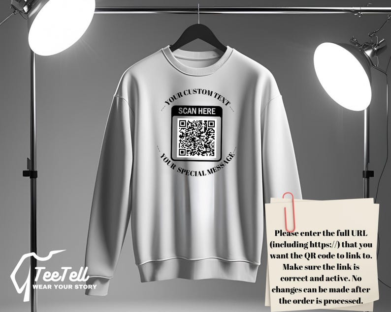 May include: White sweatshirt with a crew neck, hanging on a black hanger. The front features a QR code with the text "YOUR CUSTOM TEXT", "SCAN HERE", and "YOUR SPECIAL MESSAGE". A paper with instructions is clipped to the sweatshirt.