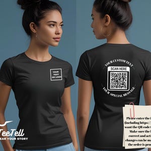 May include: Black t-shirt with a white square that says "YOUR TEXT OR LOGO" on the front. The back of the shirt has a QR code with the text "SCAN HERE" and "YOUR SPECIAL MESSAGE". The TeeTell logo is at the bottom.