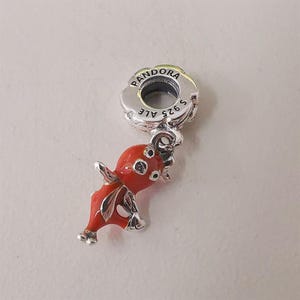 May include: A silver charm with a red enamel octopus design. The charm has a floral-shaped top with the word "PANDORA" and "S925 ALE" engraved. The octopus has detailed tentacles and is a vibrant red color.