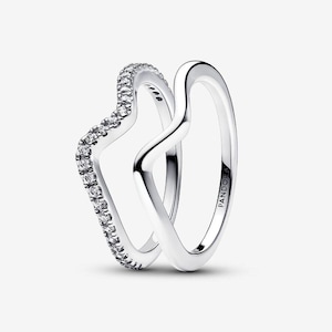 Könnte beinhalten: Zwei silberfarbene Ringe mit einem wellenförmigen V-Design. Ein Ring ist mit einer Reihe kleiner, klarer, rund geschliffener Steine am äußeren Rand besetzt, während der andere ein schlichter, polierter Ring ist. Das Wort PANDORA ist eingraviert.
