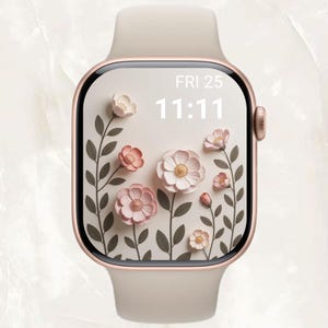 Op de afbeelding: Een roségouden smartwatch met een crèmekleurige band. De wijzerplaat toont een bloemenontwerp met roze en witte bloemen, groene stelen en de datum en tijd: VR 25 11:11.