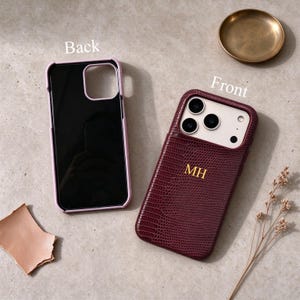 May include: Two phone cases are displayed. One is a light pink case showing the back interior. The other is a dark burgundy case with a textured crocodile pattern, featuring the gold embossed initials MH on the back and a camera cutout.