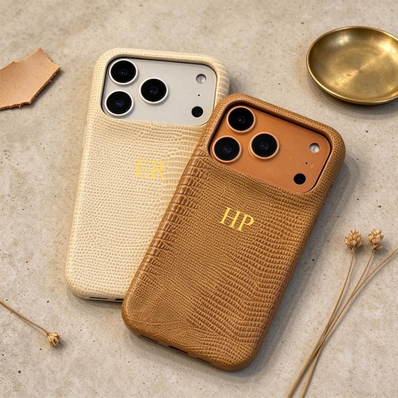 May include: Two smartphone cases with a textured lizard-skin pattern. One case is cream-colored with the gold-embossed initials ER, and the other is tan with the gold-embossed initials HP. Both feature cutouts for the camera lenses and flash.