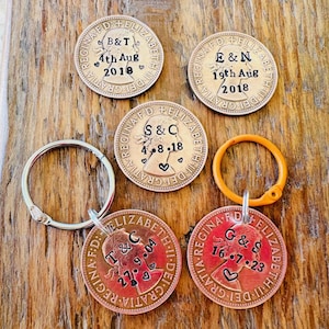 May include: Five copper-colored coins with a key ring attached to one. Each coin has a profile of a woman's face and text that reads "REGINA F.D. ELIZABETH II DEI GRATIA" and "S&C 4.8.18", "B&T 4th Aug 2018", "E&N 19th Aug 2018", "T&C 27.9.04", and "G&S 16.7.23".