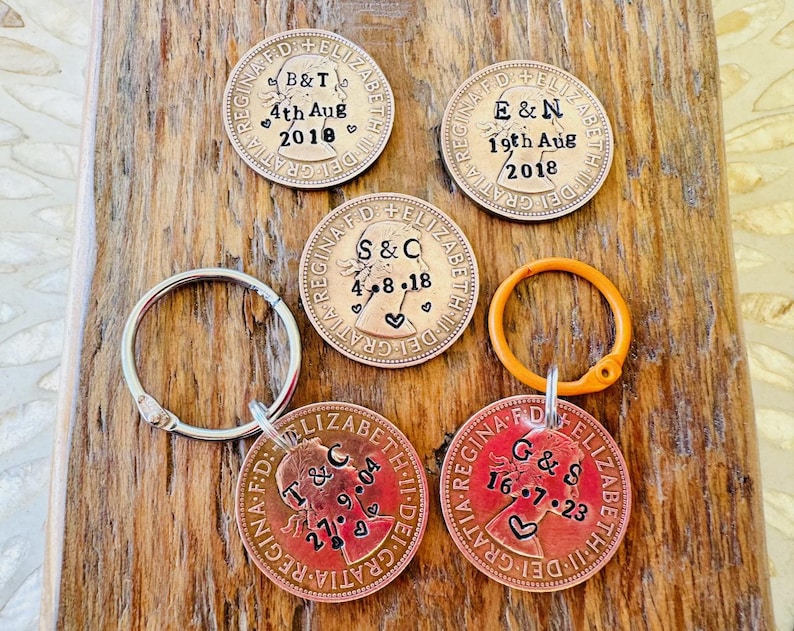 May include: Five copper-colored coins with a key ring attached to one. Each coin has a profile of a woman's face and text that reads "REGINA F.D. ELIZABETH II DEI GRATIA" and "S&C 4.8.18", "B&T 4th Aug 2018", "E&N 19th Aug 2018", "T&C 27.9.04", and "G&S 16.7.23".