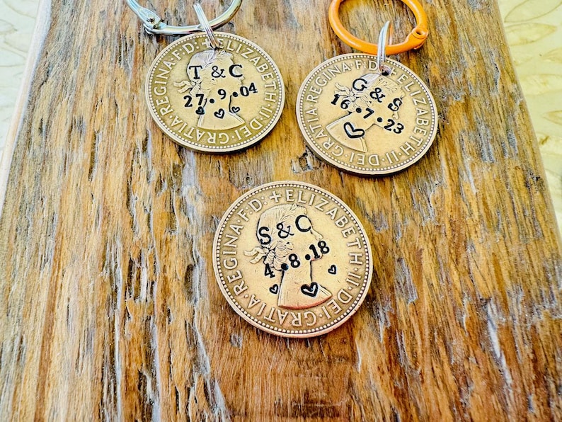 May include: Three gold-colored coins with a profile of Queen Elizabeth II on each. The coins have been personalized with initials and dates, such as "T & C 27.9.04", "G & S 16.7.23", and "S & C 4.8.18".