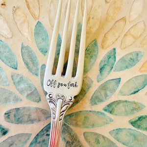 May include: A silver fork with an ornate handle. The fork has the words "Off you fork" engraved on the front.