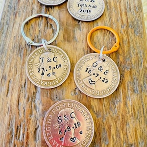 May include: Five antique British coins with a profile of Queen Elizabeth II on each. The coins are engraved with the initials of couples and their wedding dates. The coins are attached to key rings.