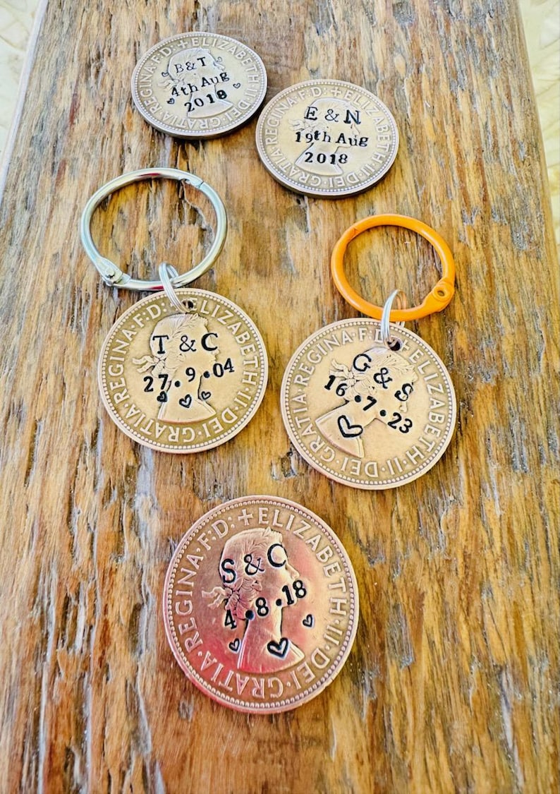 May include: Five antique British coins with a profile of Queen Elizabeth II on each. The coins are engraved with the initials of couples and their wedding dates. The coins are attached to key rings.
