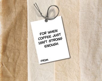 Może przedstawiać: Biała etykieta prezentowa z czarnym napisem "FOR WHEN COFFEE JUST ISN'T STRONG ENOUGH", z miejscem na "FROM:" na dole. Etykieta jest przymocowana szarą sznurkiem. Tło to mieszanka beżowych tkanin.