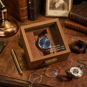 Könnte beinhalten: Eine Armbanduhr mit blauem Zifferblatt und braunem Lederarmband wird in einer Holzbox präsentiert. Auf der Box steht: „An den Mann, der mir seine Zeit geschenkt hat. Alles Gute zum Vatertag.“ Weitere Artikel sind ein Stift, eine Brille und eine Taschenuhr.