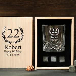 May include: A personalized whiskey glass and wooden box set. The glass and box are engraved with the number "22", the name "Robert", and a birthday message. Includes whiskey stones. The box is made of light-colored wood.