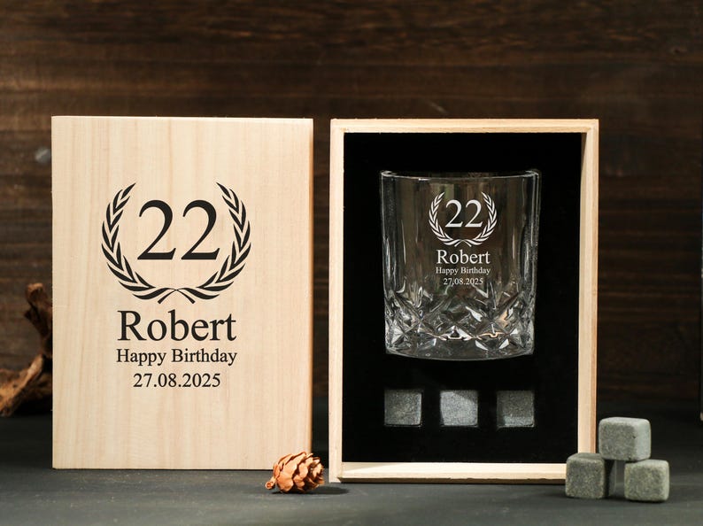 May include: A personalized whiskey glass and wooden box set. The glass and box are engraved with the number "22", the name "Robert", and a birthday message. Includes whiskey stones. The box is made of light-colored wood.