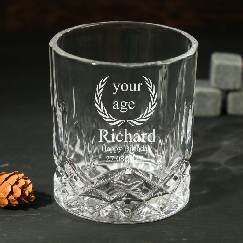 May include: A clear, faceted glass tumbler with the text "your age" inside a laurel wreath, the name "Richard", and "Happy Birthday 27.08.2022" etched on the front. The glass has a diamond pattern on the lower half.
