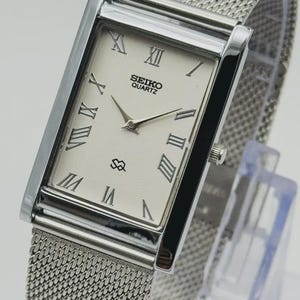 Könnte beinhalten: Eine rechteckige Seiko Quartz-Uhr mit einem silbernen Mesh-Armband. Das Zifferblatt ist cremefarben mit schwarzen römischen Ziffern und Zeigern. Die Uhr hat eine silberne Lünette und das Seiko Quartz-Logo.