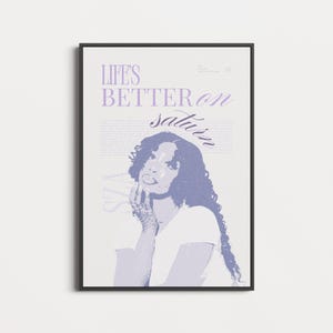 May include: A framed art print with a purple and white design. The image features a person with long, wavy hair and the text "LIFE'S BETTER ON saturn". The artwork is in a black frame, suitable for wall display. The print is in a portrait orientation.