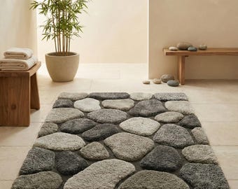 May include: A rectangular bath mat with a stone design. The mat features various shades of grey, mimicking the appearance of river stones. The stones are arranged closely together, creating a textured surface. The rug is designed for bathroom use.