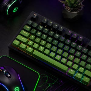 Könnte beinhalten: Eine schwarze mechanische Tastatur mit olivgrünen Tastenkappen und weißer Beschriftung, beleuchtet durch integrierte RGB-Beleuchtung. Die Tastatur umfasst Standard-QWERTY-Tasten, Funktionstasten und eine Leertaste auf einer dunklen Oberfläche.