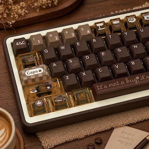 May include: A mechanical keyboard with brown keycaps and transparent accent keys. The keyboard has a brown frame with white trim. The keycaps have white lettering. The space bar reads "It's not a bug it's".