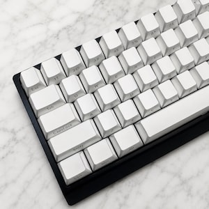 May include: A white mechanical keyboard with a black surround. The keycaps are white with black lettering. The keyboard layout includes standard keys like Tab, Shift, Ctrl, and Alt.