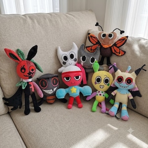 May include: A collection of eight colorful plush toys featuring various cartoon-inspired characters with distinct shapes, including a butterfly, a red and black creature, a yellow figure with polka dots, and a horned white character.