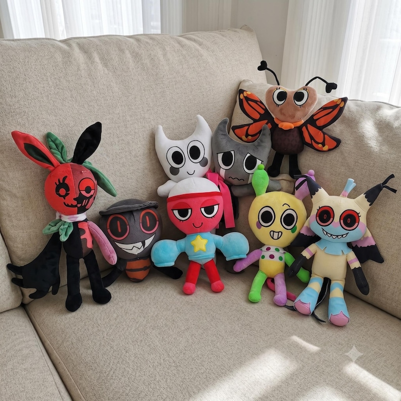 May include: A collection of eight colorful plush toys featuring various cartoon-inspired characters with distinct shapes, including a butterfly, a red and black creature, a yellow figure with polka dots, and a horned white character.