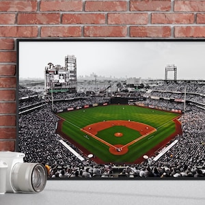May include: A framed wall art print featuring a high-angle, selective color photograph of a baseball stadium. The field is vibrant green with a reddish-brown dirt infield, while the surrounding stands and city skyline are rendered in black and white.