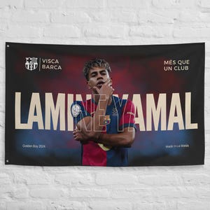 Puede incluir: Una bandera negra con un retrato de Lamine Yamal, y el nombre "LAMINE YAMAL" en letras blancas grandes. La bandera incluye el escudo del FC Barcelona y las frases "Visca Barca", "Més que un club", "Golden Boy 2024" y "Made in La Masia".