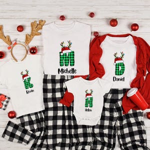 May include: A collection of Christmas-themed family pajamas and accessories. The white shirts feature a green plaid letter design with a Santa hat and reindeer antlers. The names "Kevin", "Michelle", "Daniel", and "Helen" are printed on the shirts.