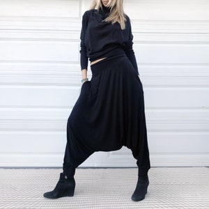 Puede incluir: Una mujer con una blusa negra de cuello alto y pantalones de har&eacute;n negros. Los pantalones tienen una pierna ancha y una cintura fruncida.