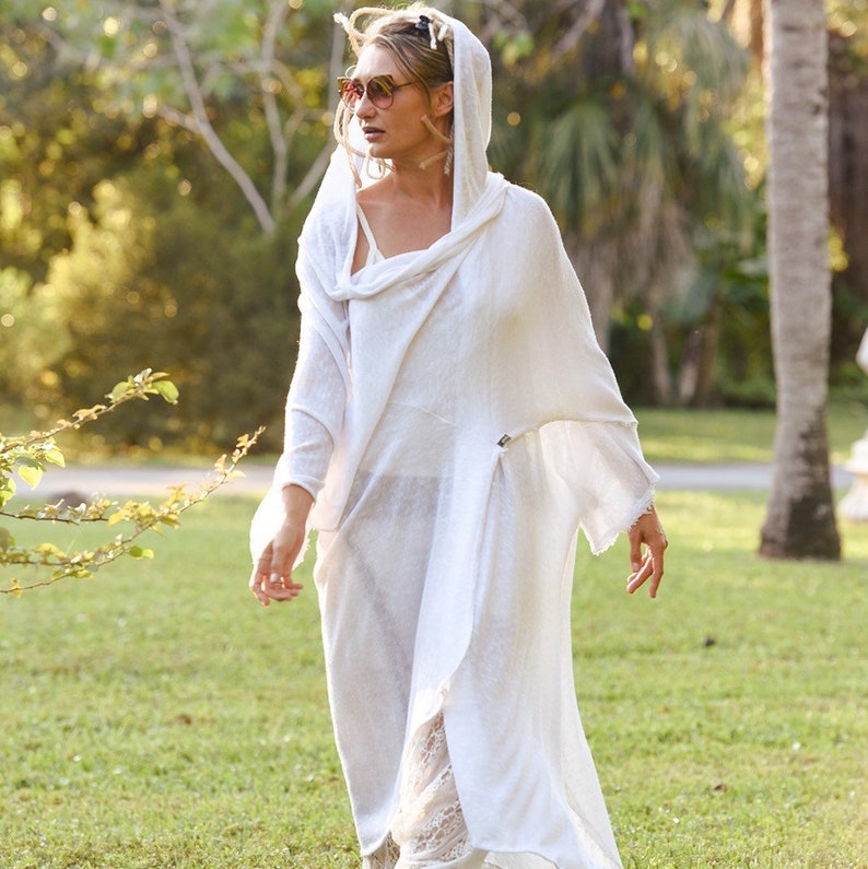 May include: A white hooded tunic with a loose, flowing fit. The tunic is made of a lightweight fabric and has a relaxed, casual style.