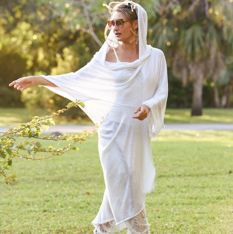 May include: A white hooded tunic with a loose, flowing fit. The tunic is made of a lightweight fabric and has a relaxed, casual style.