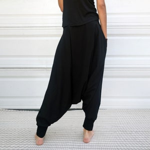 May include: Black harem pants with a wide leg and a gathered waist. The pants are made of a soft, comfortable fabric and have a relaxed fit.