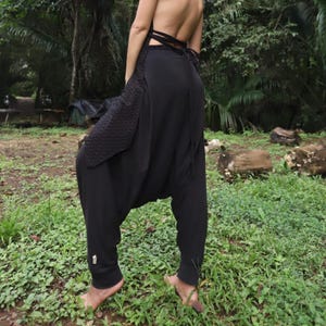 May include: Black harem pants with a loose, flowing fit. The pants have a unique design with a gathered waist and a wide leg.