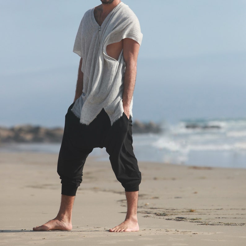 May include: A person wearing a gray, loose-fitting shirt with a zipper and black, loose-fitting pants. The person is standing on a sandy beach.