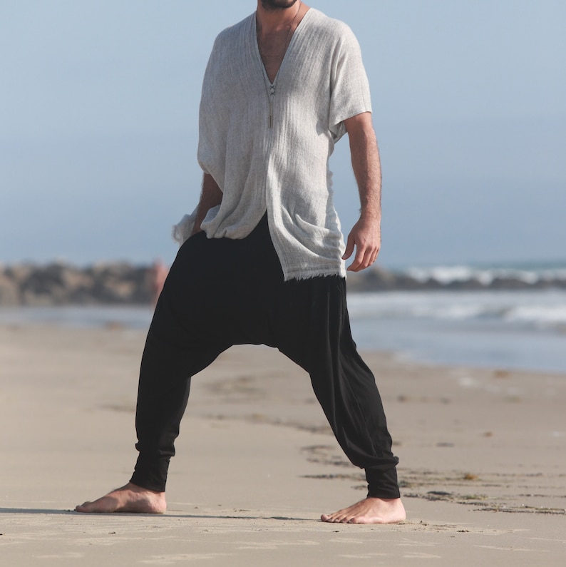 May include: A person wearing a light gray, long-sleeved shirt with a zipper and black pants. The person is standing on a sandy beach.
