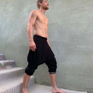 May include: A person wearing black harem pants with a loose, flowing fit. The pants are cropped at the knee and have a wide, comfortable waistband.