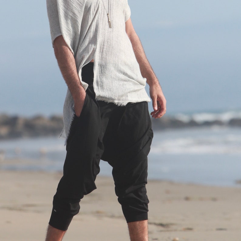 May include: A person wearing a white, loose-fitting top and black, cropped pants. The pants have a unique, gathered design at the ankles.