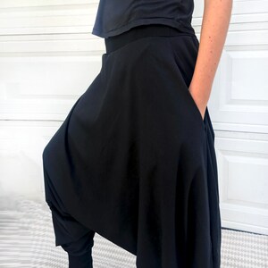 May include: Black, loose-fitting pants with a wide, flowing leg and a high waist. The pants have a unique, draped design and a single pocket on the side.