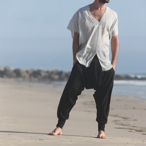May include: A person wearing a white, loose-fitting shirt with a V-neck and black pants. The pants have a wide leg and are gathered at the ankles.