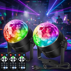 May include: Two black stage lights with multi-colored, faceted, hexagonal-patterned domes. Each light is mounted on an adjustable bracket and includes a power cord. Three identical black remote controls with various buttons are displayed in the foreground.