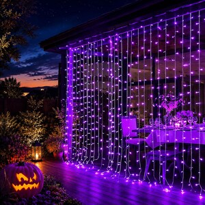 May include: A curtain of purple LED string lights hanging from the edge of a roof, illuminating a wooden deck. A carved jack-o'-lantern with a glowing interior sits on the deck, while a dining table with chairs is visible behind the light strands.