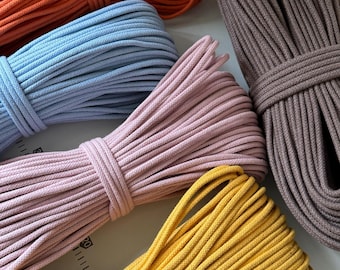 May include: A collection of colorful macrame cords in various hues. The image showcases bundles of orange, light blue, pink, yellow, and brown cords. Each cord is neatly coiled and bound, highlighting the texture and color variations. Ideal for crafting and DIY projects.