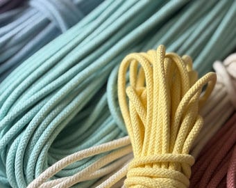May include: Close-up of several bundles of colorful macrame cord in shades of lavender, blue, yellow, cream, and pink. The cords are tightly wound and ready for crafting projects. The image highlights the texture and variety of colors.