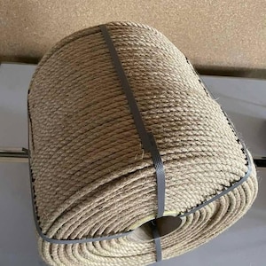 May include: A tightly coiled roll of natural-colored rope, secured with two gray plastic straps. The rope appears to be made of a thick, fibrous material, likely jute or sisal, and is tightly wound. The texture of the rope is visible, with individual strands creating a textured surface.