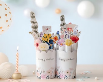 May include: Two white paper flower vases with scalloped edges, each with a floral arrangement and the words "Happy Birthday." The vases are decorated with watercolor flowers. A lit candle and a balloon are in the background.