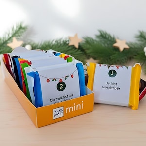 May include: An orange box of mini chocolate bars with white wrappers. The wrappers have numbers and text in German, with festive Christmas decorations. The box is labeled "Ritter Sport mini".